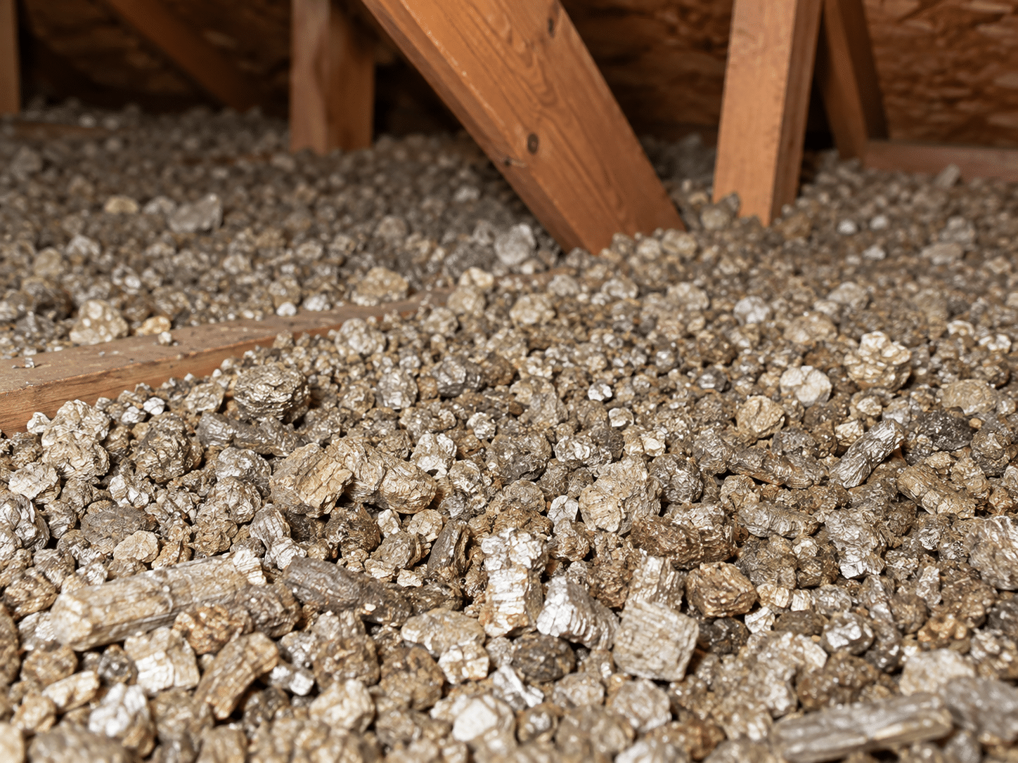 Close-up of loose-fill vermiculite insulation between wooden rafters in a residential attic.